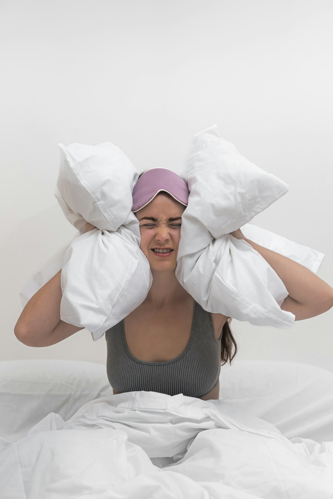 woman covers her ears with pillows, unable to sleep, enduring a throbbing headache and insomnia.